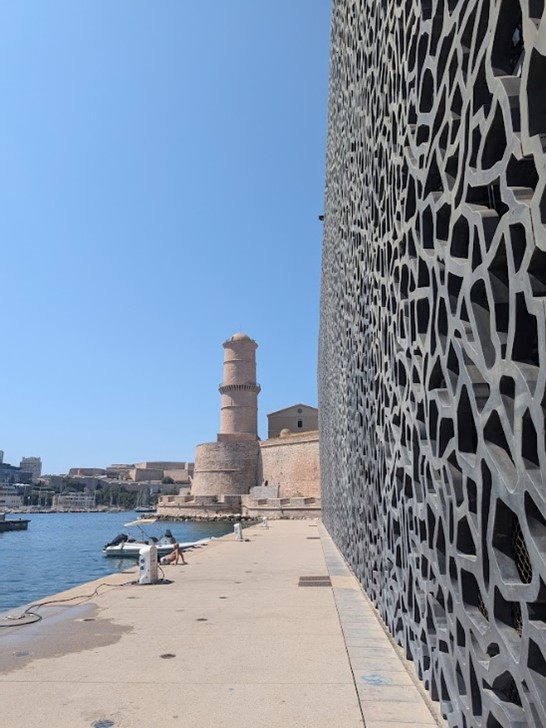 A view of Marseille's Vieux-Port, in the foreground, the Mucem, which chronicles thousands of years of Mediterranean history. A man reposes by his boat in between the two