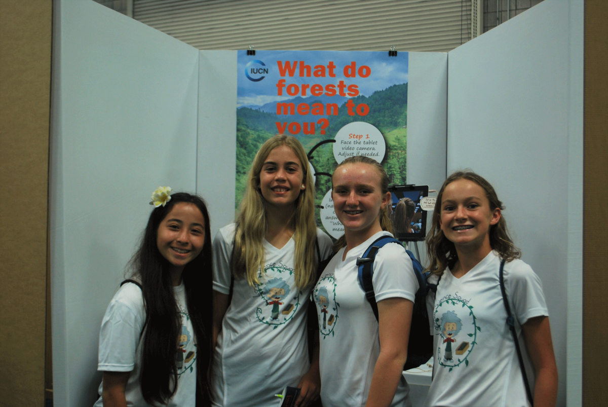 Four girls smiling at the camera with a poster behind