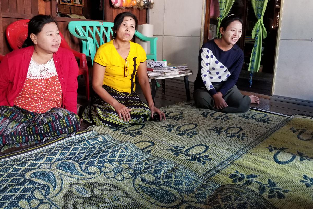 Three women sit on patterned carpets on the floor during a meeting