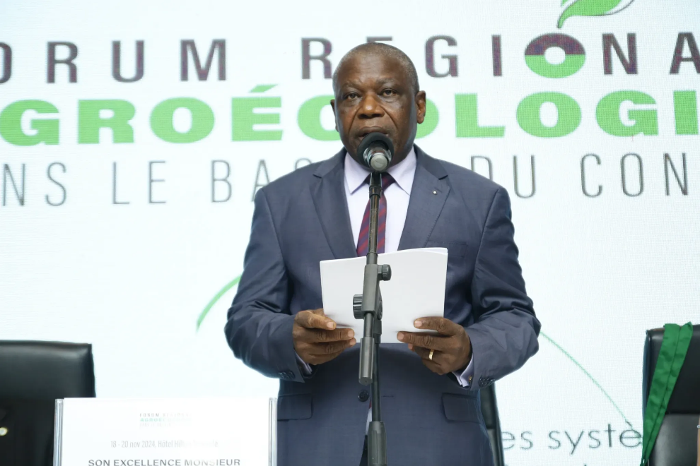 A person in a suit holding a microphone and paper

Description automatically generated