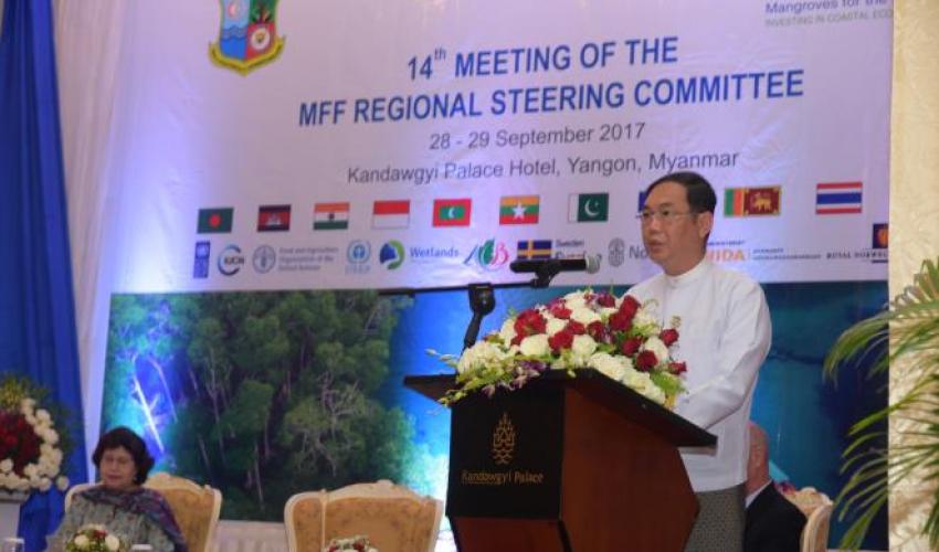 A man stands at a podium in front of a banner for the 14th Meeting of the MFF Regional Steering Committee