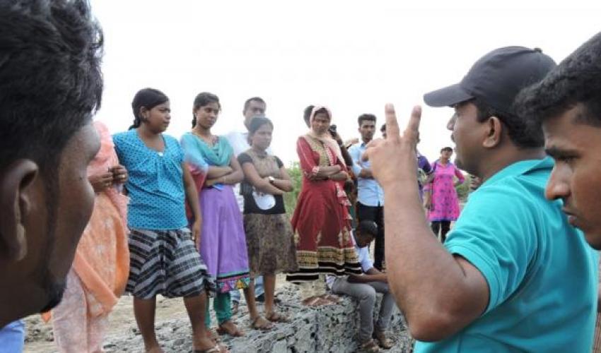 An trainer gives instruction to a group of young women standing on a stone wall