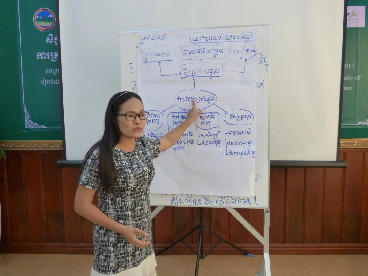 A woman points to a flow chart in Khmer drawn on large white paper