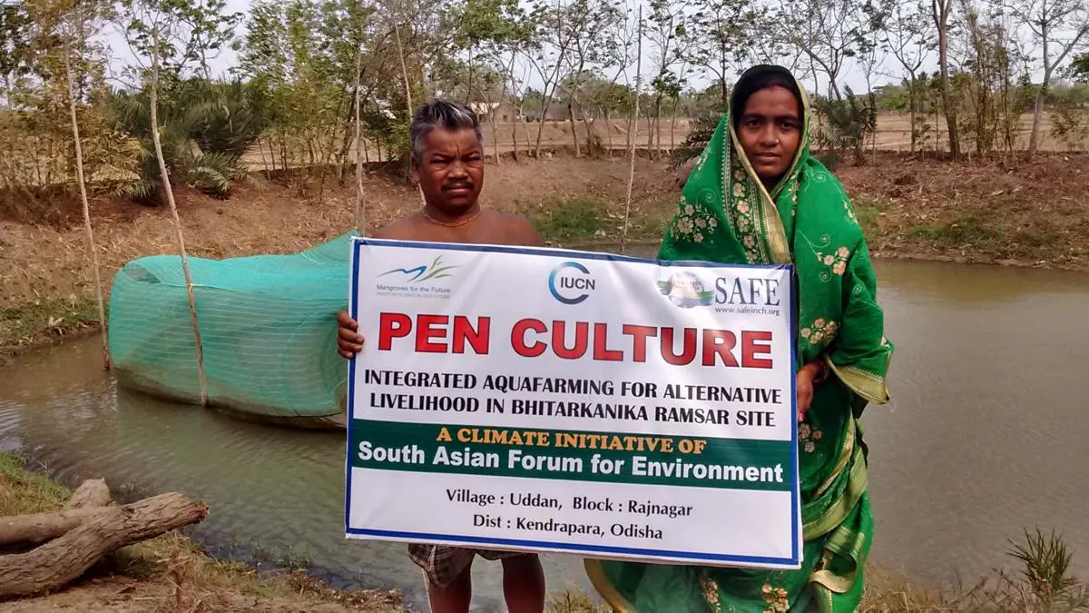 A woman in a green sari and a man hold up a sign that reads 'pen culture' in red lettering
