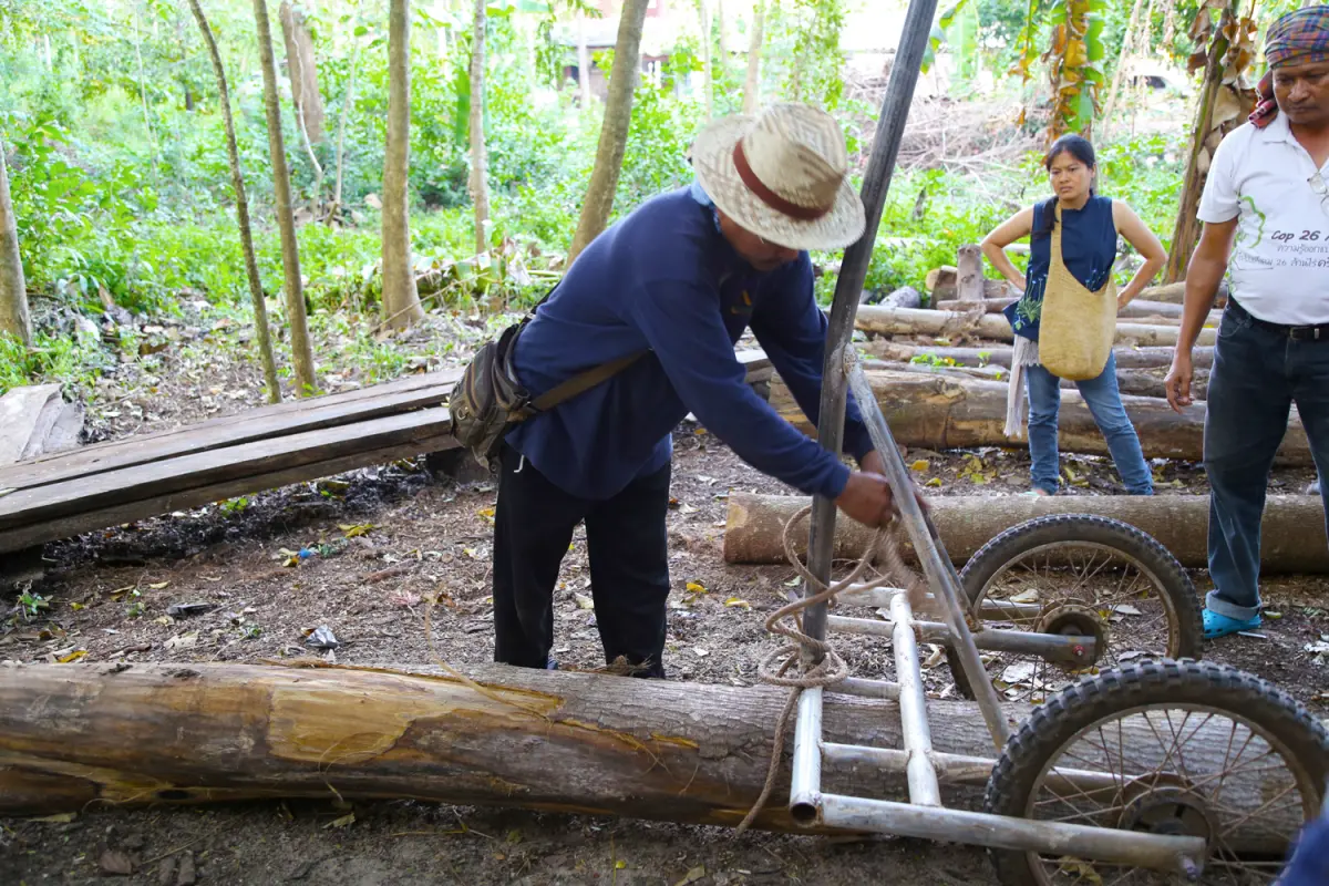 Man with hat moves log with a simple wheeled machine
