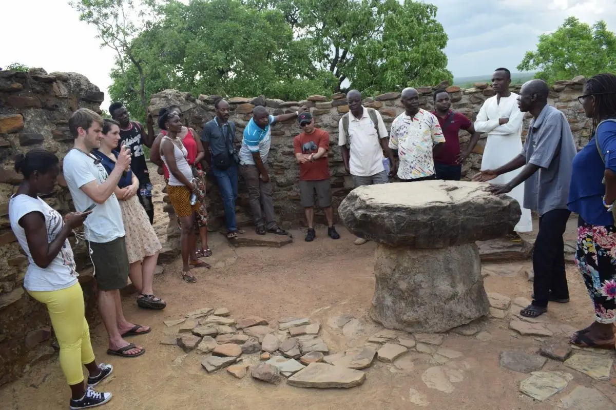 People standing and gathered around a round stone table 